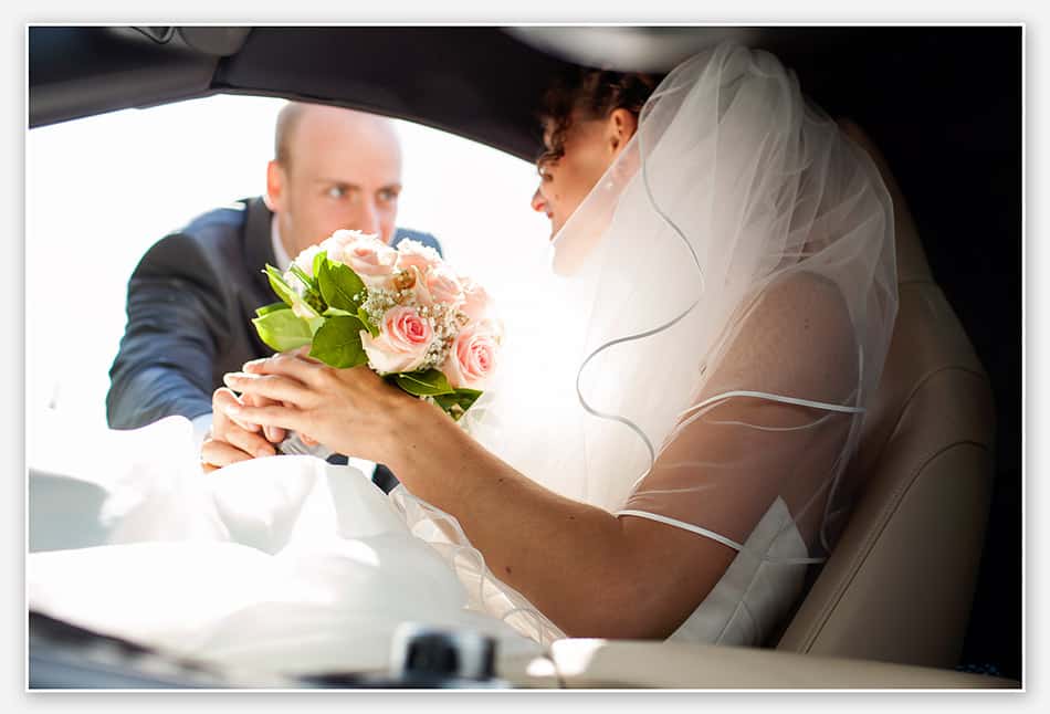 Bruidegom helpt bruid in de  trouwauto
