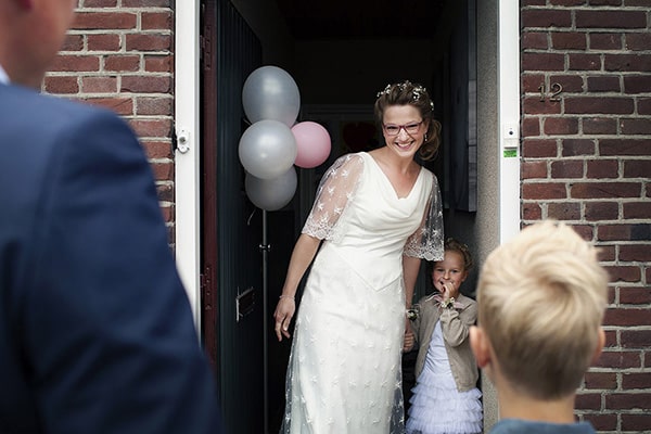Trouwfotografie_Soulmates Images_15_bruid en bruidsmeisje openen de deur voor de bruidegom