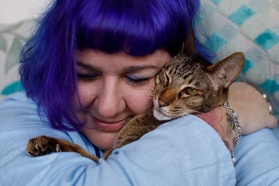 Vrouw met paars haar knuffelt liefdevol met haar kat